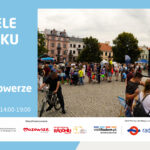Plakat informacyjny wydarzenia „Niedziele na Rynku 2026”. Program: 19 lipca – Lato na rowerze. Miejsce: Rynek, zapraszamy w godz. 14:00-19:00. Prawa część plakatu zawiera zdjęcie przedstawiające tłum ludzi uczestniczących w festynie plenerowym na brukowanym rynku miejskim. Na pierwszym planie po lewej stronie widoczny jest mężczyzna prowadzący rower, a po prawej stronie grupa ludzi stojąca przy pomniku i stoiskach. W tle zabytkowe kamienice i drzewa. Na dole logotypy organizatorów i partnerów.